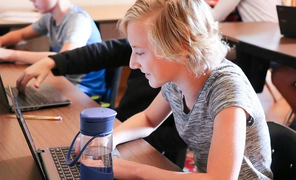 Una studentessa della Accelerated School lavora concentrata a un laptop in aula insieme ad altri studenti.