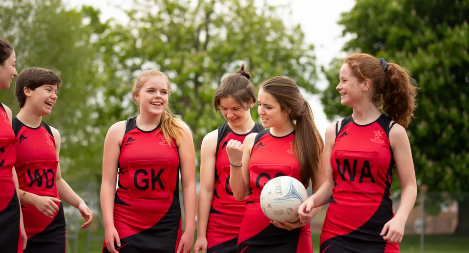 Un gruppo di giovani atlete in maglia rossa con un pallone da rugby nel campus della St. Peters School.