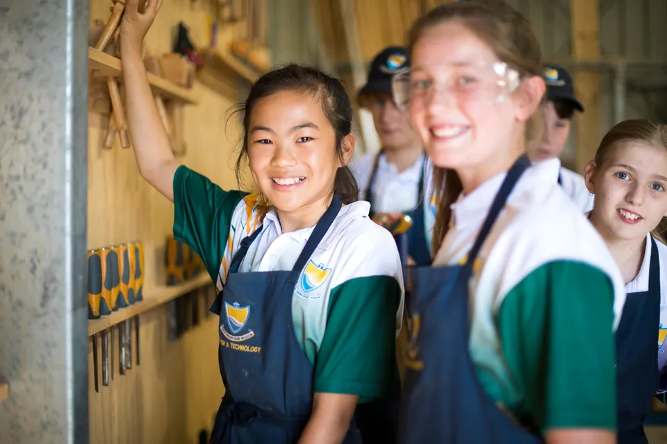 Studentesse della Esperance Anglican Community School indossano grembiuli e occhiali protettivi in un laboratorio con utensili.