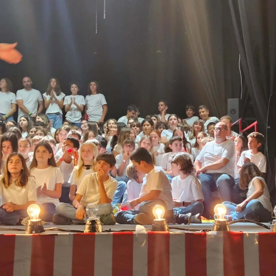 Gli studenti del Novaschool Añoreta College con magliette bianche siedono su un palco teatrale.