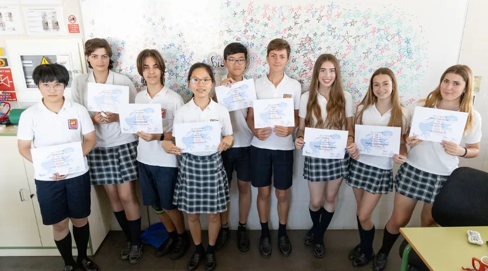 Studenti del Caxton College sono insieme in classe e mostrano dei certificati davanti a una lavagna colorata.