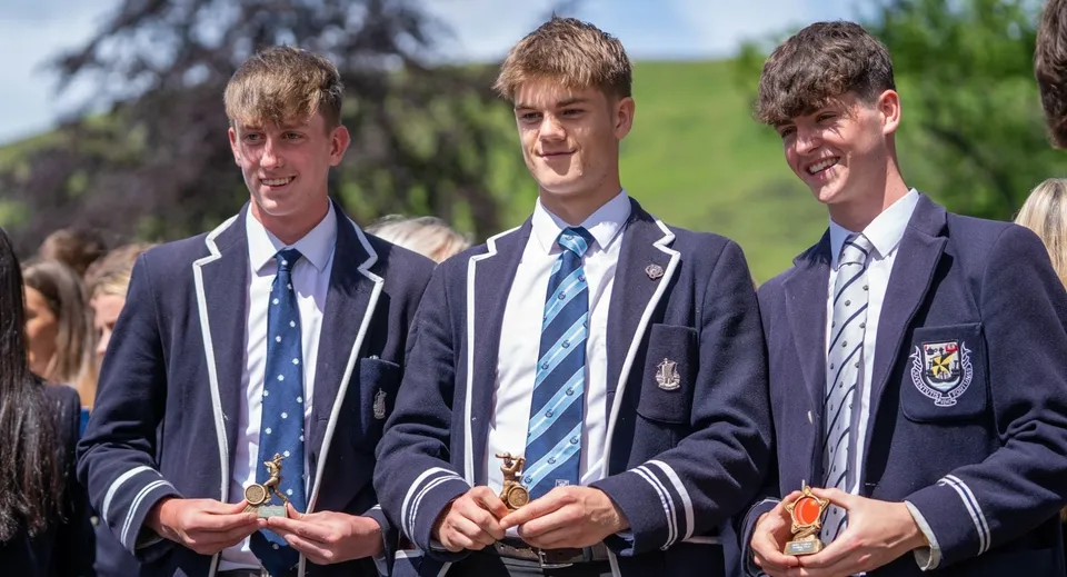 Tre studenti della Dollar Academy sono insieme su un prato con degli alberi sullo sfondo.