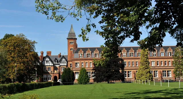 Das historische Backsteingebäude auf dem grünen Campus der Dean Close School mit gepflegtem Rasen im Vordergrund.