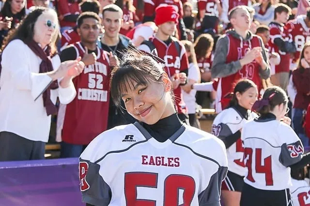 Una joven con una camiseta blanca de los Eagles está ante un grupo de personas con camisetas rojas en el campus de la Layton Christian Academy.