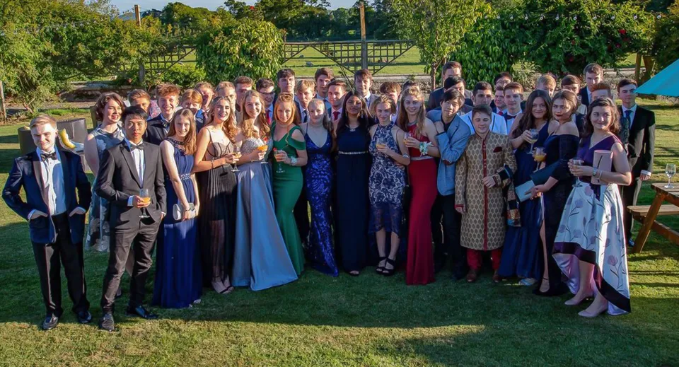 Un grande gruppo di studenti e studentesse in abito formale si trova su un prato nel campus della Oswestry School.