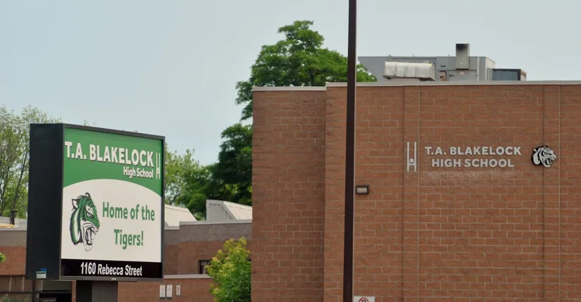 L'edificio in mattoni della Thomas A. Blakelock High School con un cartello 'Home of the Tigers' in primo piano è circondato da alberi.