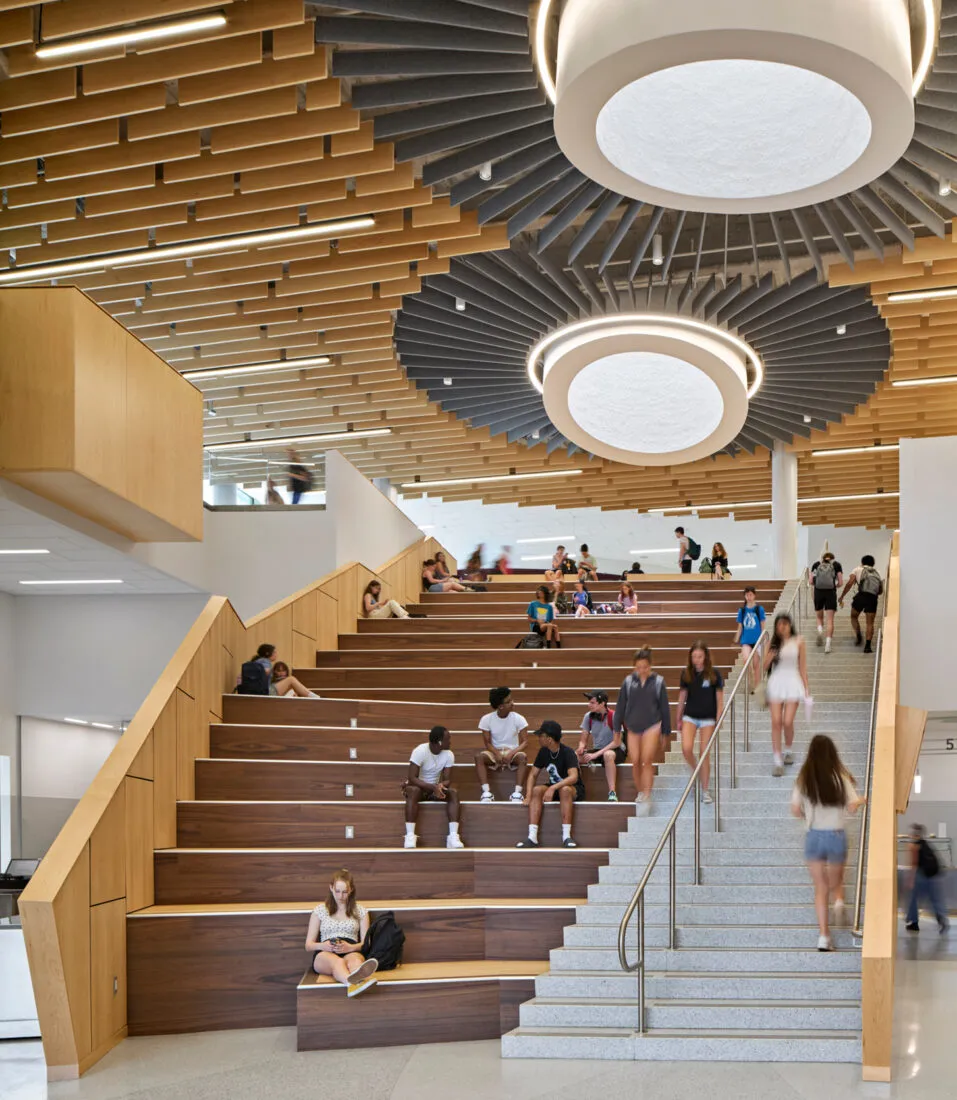 Estudiantes sentados y caminando en una amplia escalera de madera en el interior de Arlington High School.