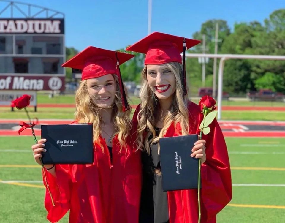 Due diplomate della Mena High School sono in piedi sul campo sportivo con in mano i loro diplomi.
