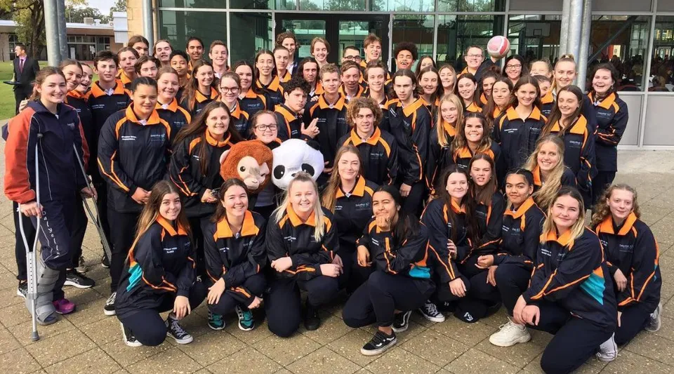 Un gruppo di studenti del Dalyellup College indossa le divise abbinate nere e arancioni davanti a un moderno edificio in vetro.