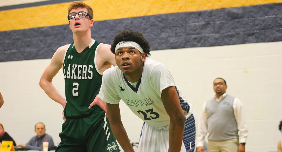 Due giocatori di pallacanestro della Erie First Christian Academy e di una squadra avversaria guardano in alto durante una partita.
