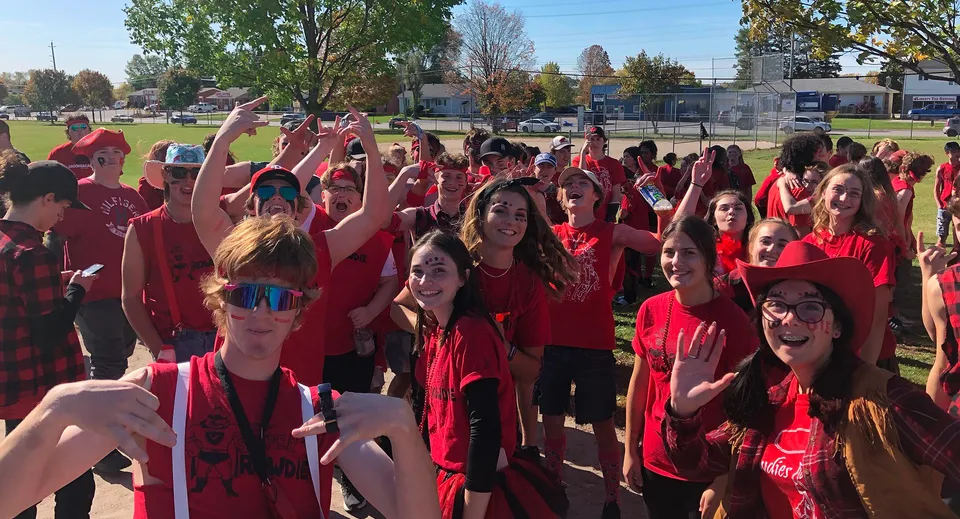 Un gruppo di studenti e studentesse della Elmvale District High School indossa t-shirt rosse e alza le braccia esultando su un campo.