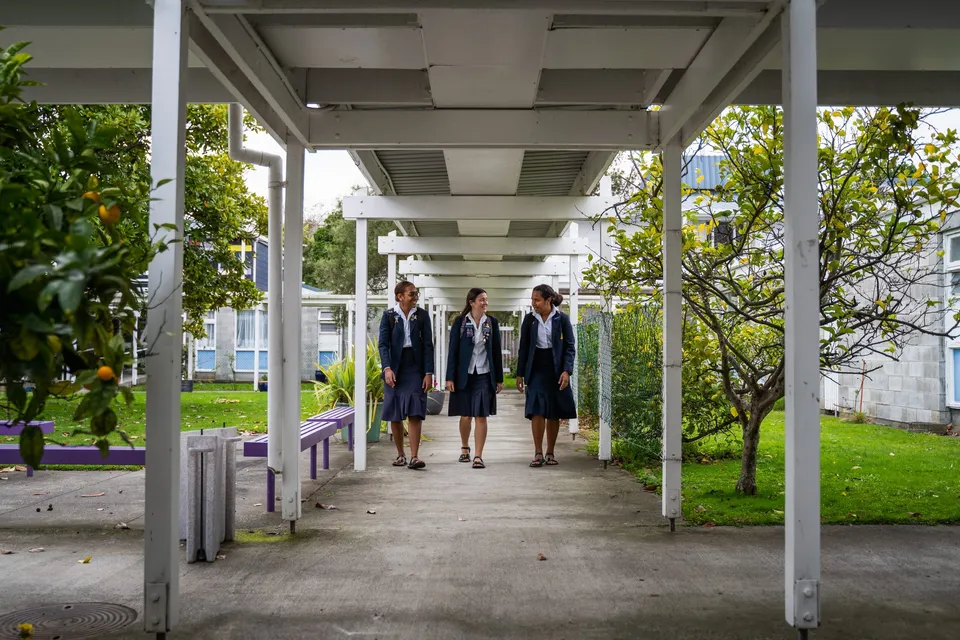 Studentesse in abiti formali camminano su un percorso coperto nel campus del Whanganui Girls’ College, circondato da aree verdi e alberi.