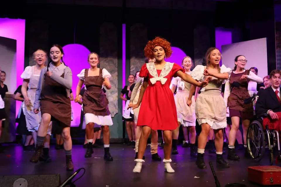 Sul palco del Clonfert College diversi studenti e studentesse si esibiscono durante uno spettacolo con luci colorate.
