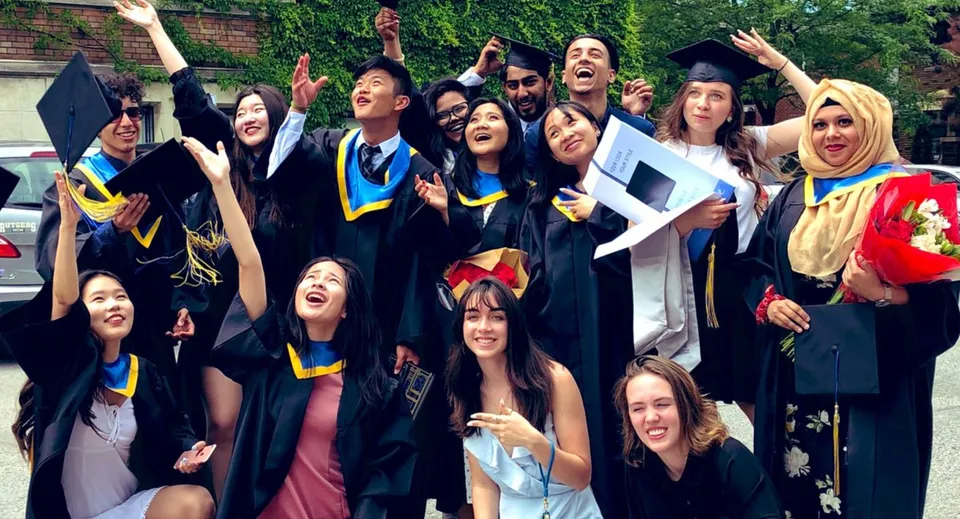 Un gruppo di diplomati in toghe colorate festeggia davanti a un edificio in mattoni nel campus del Glebe Collegiate Institute.