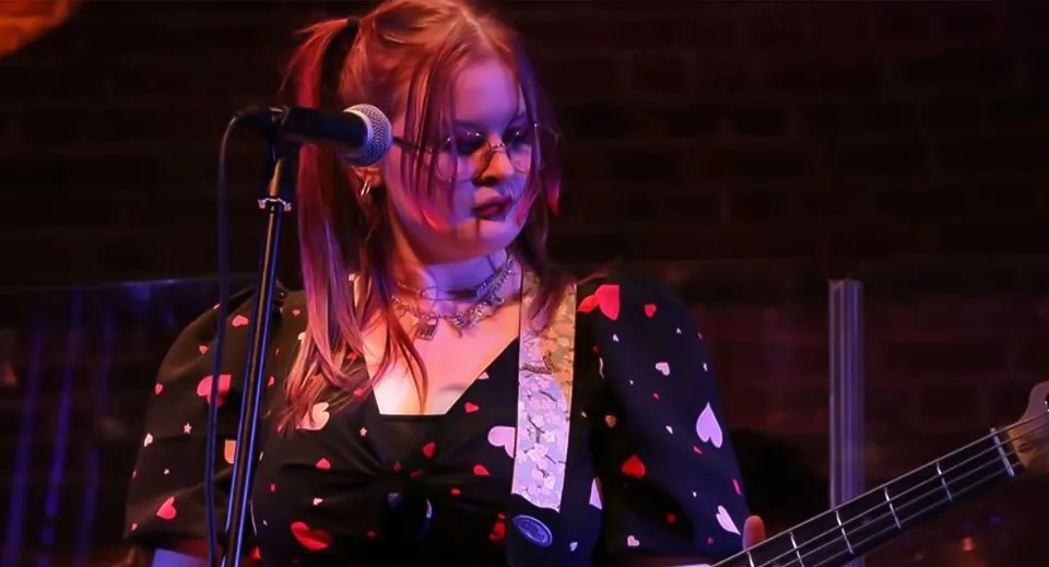Una studentessa del Boston College suona la chitarra e canta su un palco illuminato a colori.