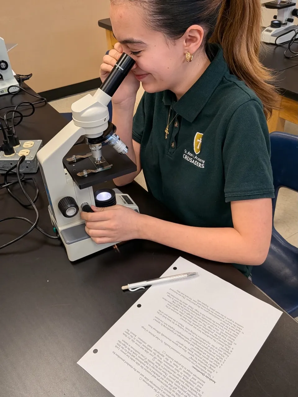 Una studentessa della St Ann's Academy guarda attraverso un microscopio al tavolo.