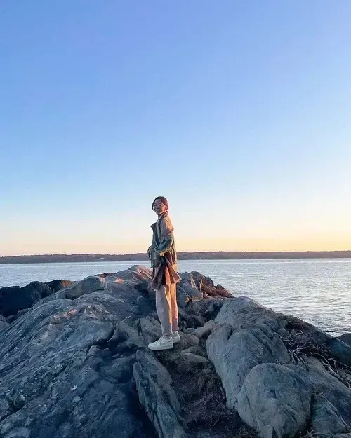 Chica de pie sobre las rocas a la orilla del mar al atardecer