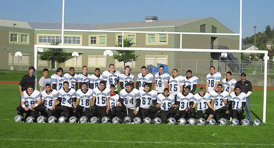 Un gruppo di studenti in divisa da calcio posa sul campo sportivo davanti all'edificio scolastico della Moscrop School.