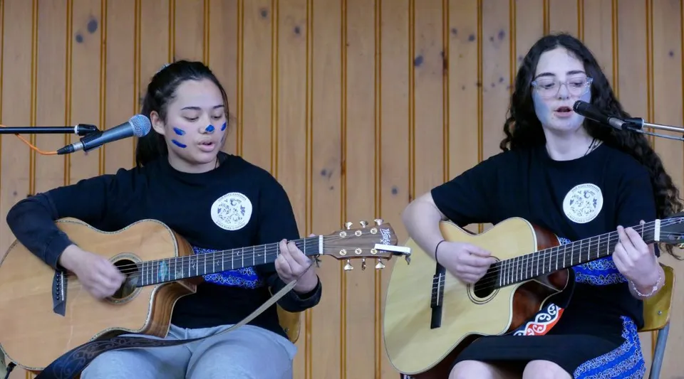 Due studentesse suonano chitarre acustiche e cantano in una stanza rivestita in legno al Blue Mountain College.