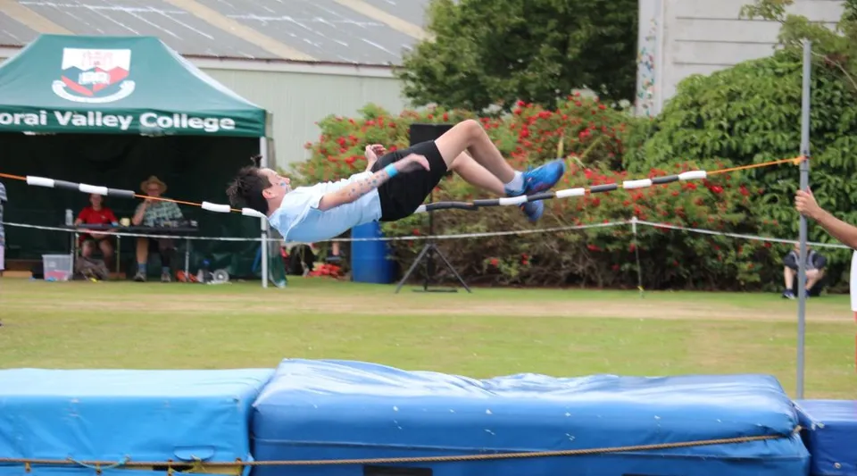 Una studentessa del Kaikorai Valley College esegue un salto in alto su un campo erboso davanti allo striscione del college.