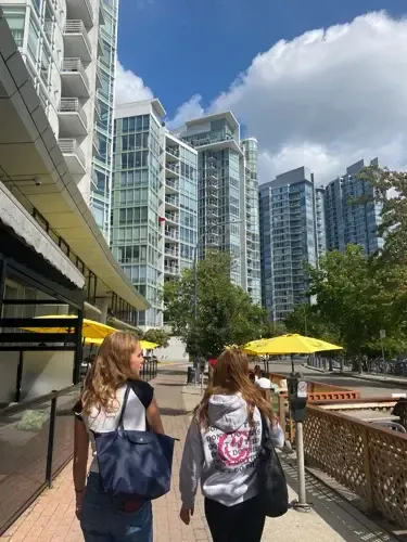 Dos chicas paseando de espaldas por una calle con rascacielos y sombrillas amarillas