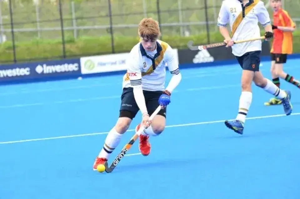 Uno studente della Whitgift School gioca a hockey su prato sul campo in erba sintetica blu con altri giocatori sullo sfondo.