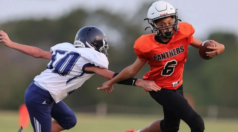 Due giocatori di calcio in maglia rossa e blu giocano sul campo della TMI Episcopal School.