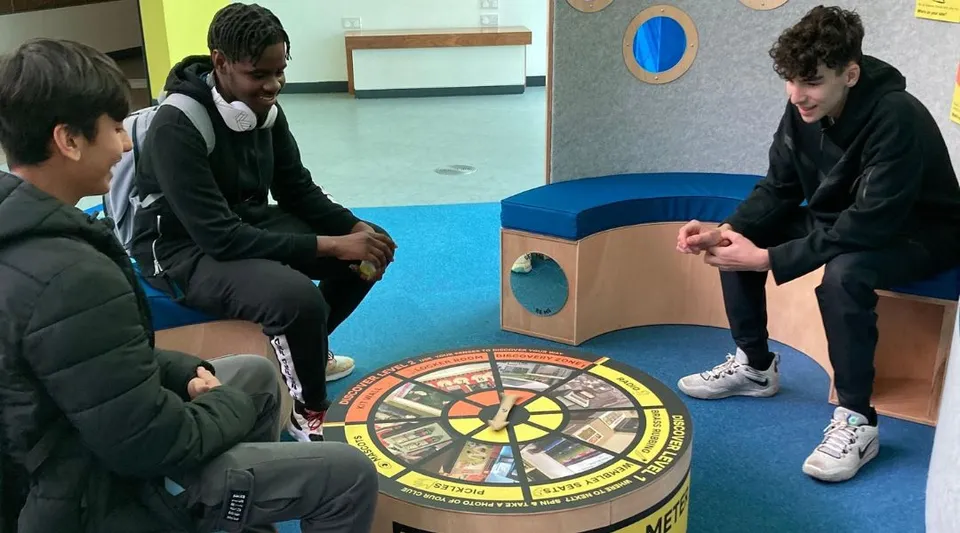 Studenti dell'Abbey College Manchester si radunano attorno a un grande tabellone da gioco rotondo sul pavimento per un'attività cooperativa.