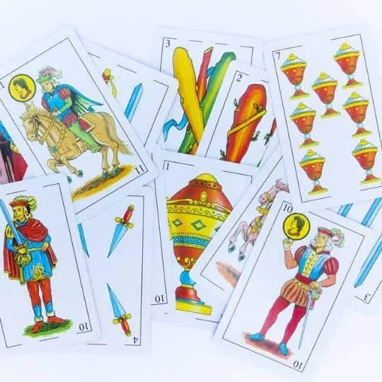 Varias cartas de una baraja española extendidas y superpuestas sobre un fondo blanco