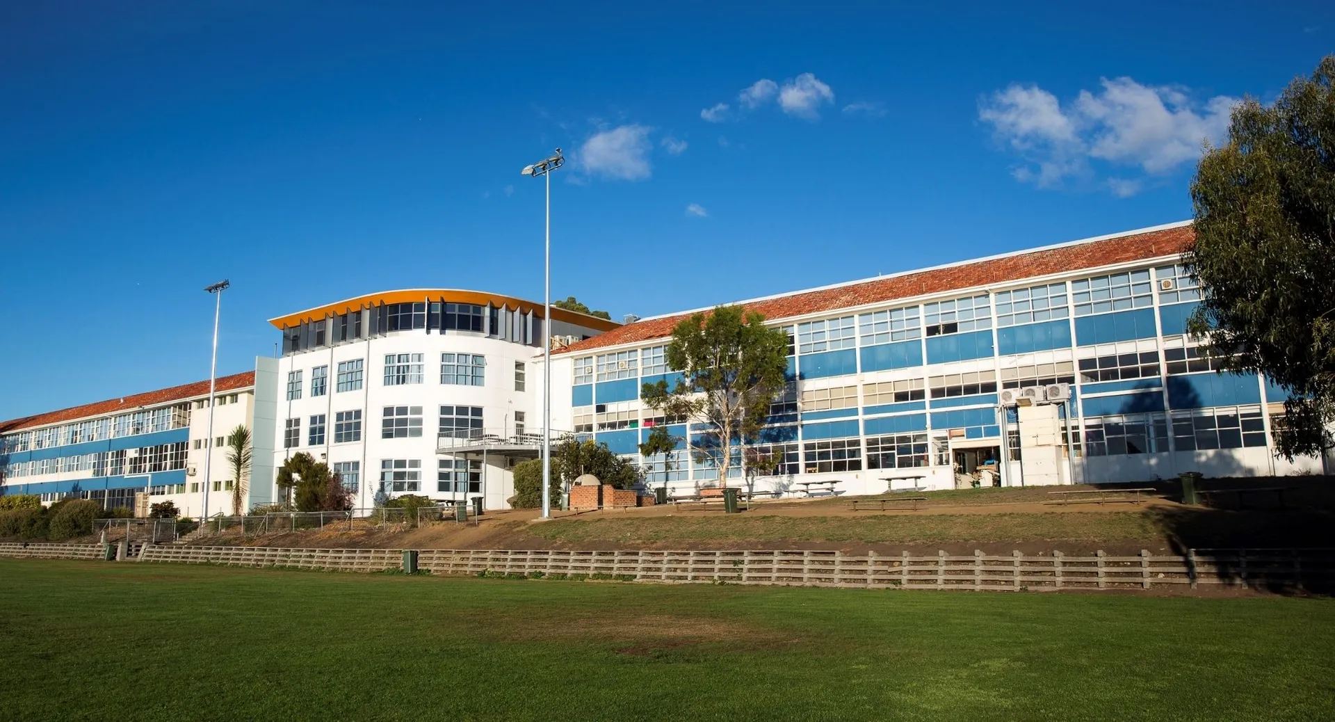 L'edificio a più piani della Taroona High School mostra moderne facciate in vetro e mattoni sotto un cielo blu.