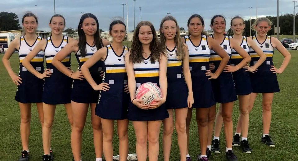 Un gruppo di giovani atlete si trova insieme sul campo sportivo della Coolum State High School sotto un cielo nuvoloso.
