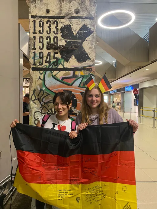 Due studentesse con la bandiera tedesca davanti a un segmento del Muro di Berlino