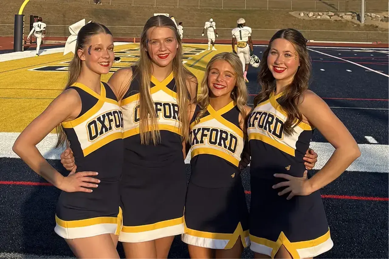 Quattro cheerleader in divisa Oxford sorridono a bordo del campo da football