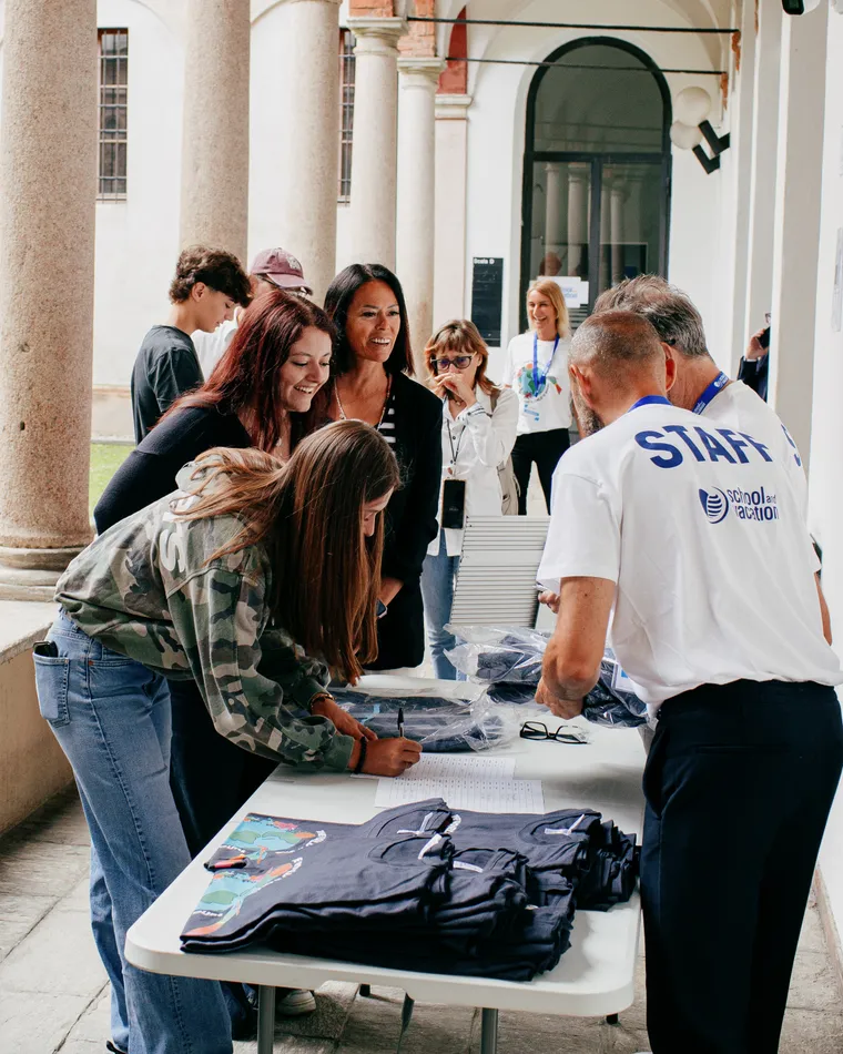 Gruppo di persone sotto un porticato registra i partecipanti a un evento a un banco con magliette