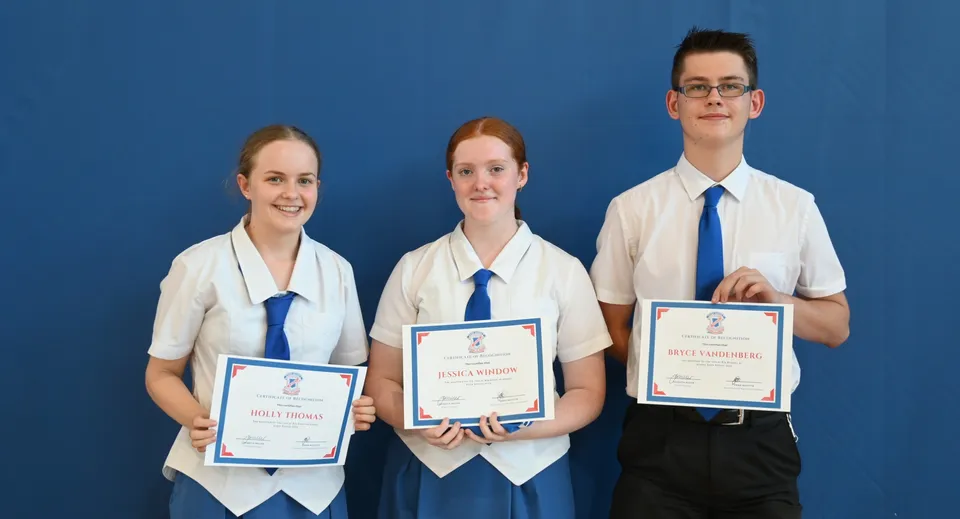 Tre studenti della Aspley State High School tengono insieme i loro certificati davanti a uno sfondo blu.