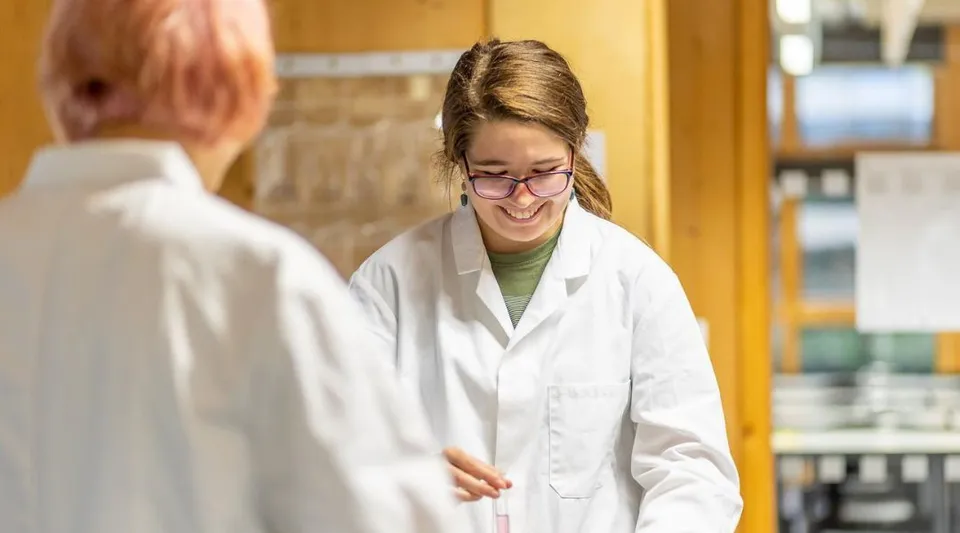 Una giovane donna in camice bianco da laboratorio sorride nel laboratorio della Bath Academy.
