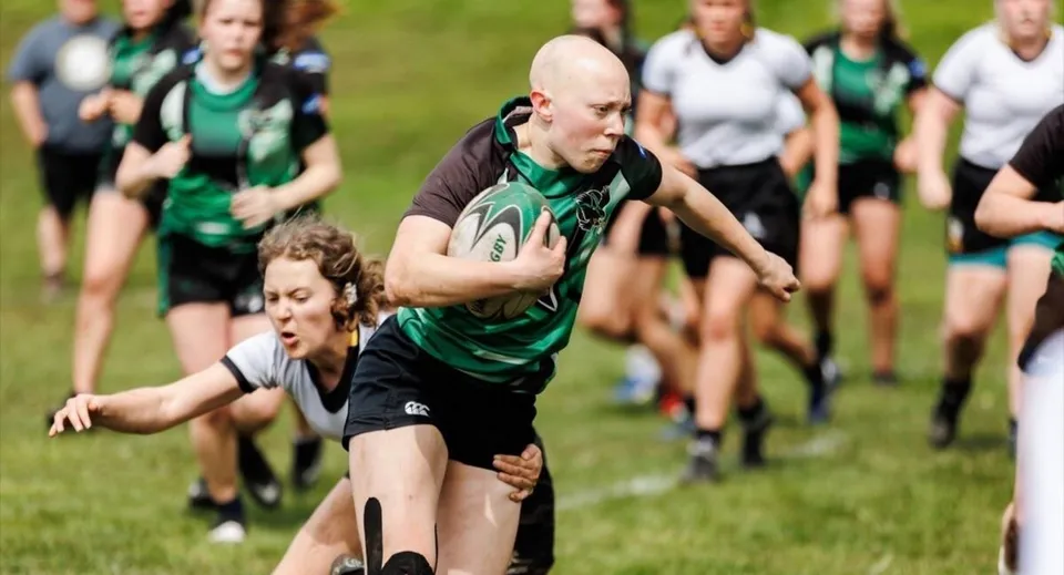Studenti della Prospect High School giocano una partita di rugby su un campo erboso durante una fase di placcaggio.