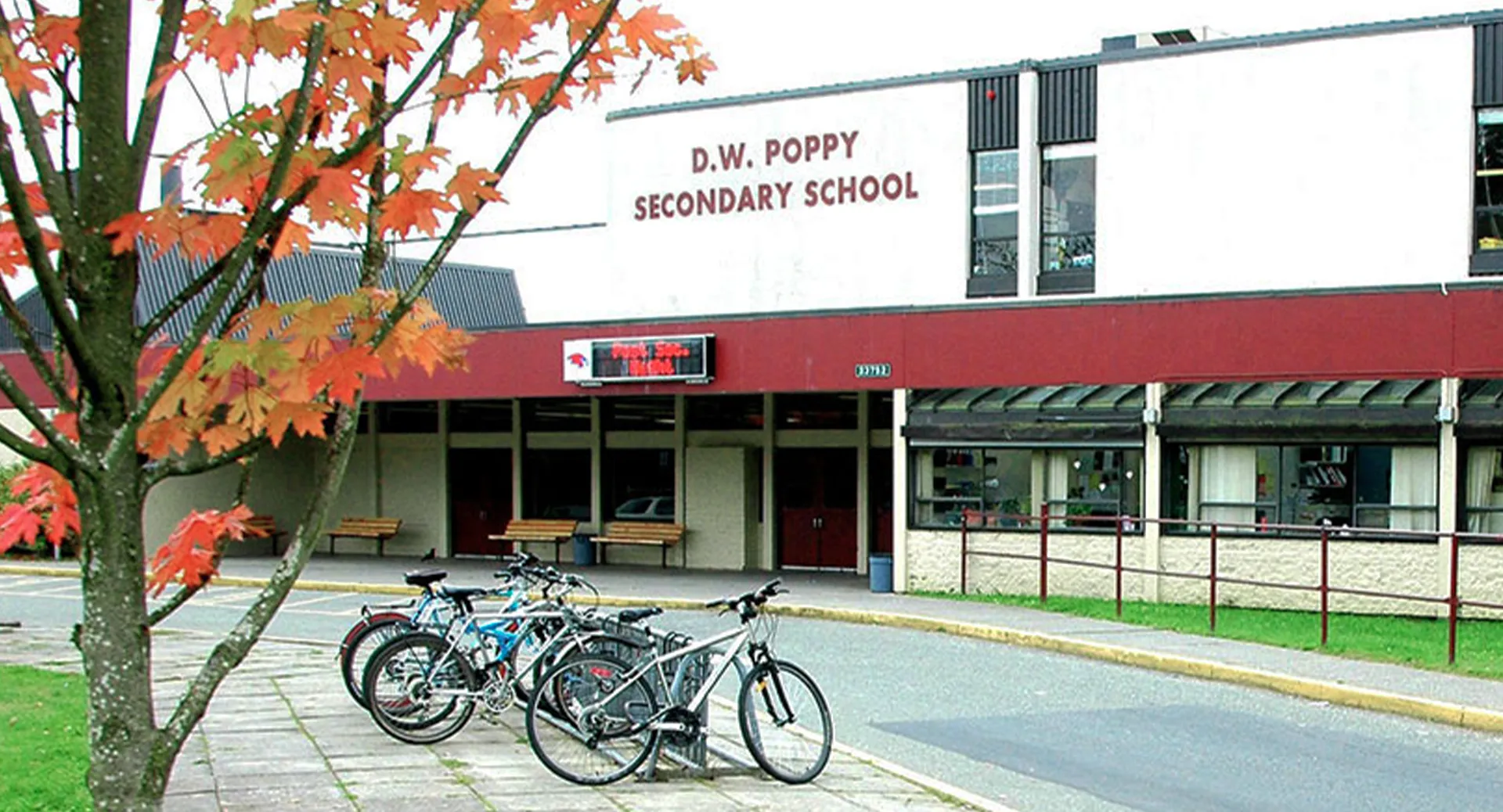 L'edificio della D.W. Poppy Secondary School in autunno, con foglie colorate e biciclette parcheggiate davanti.