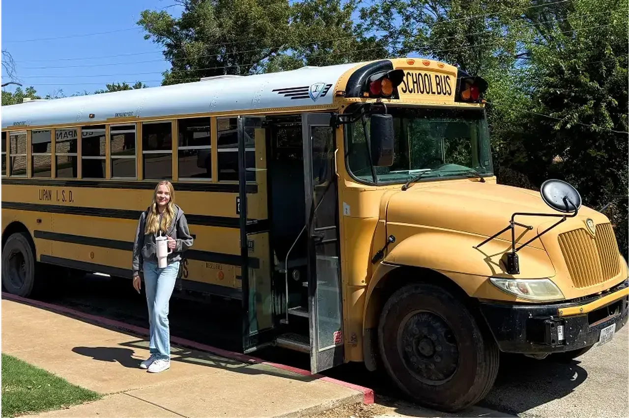 Studentessa accanto a uno scuolabus giallo americano con in mano una borraccia