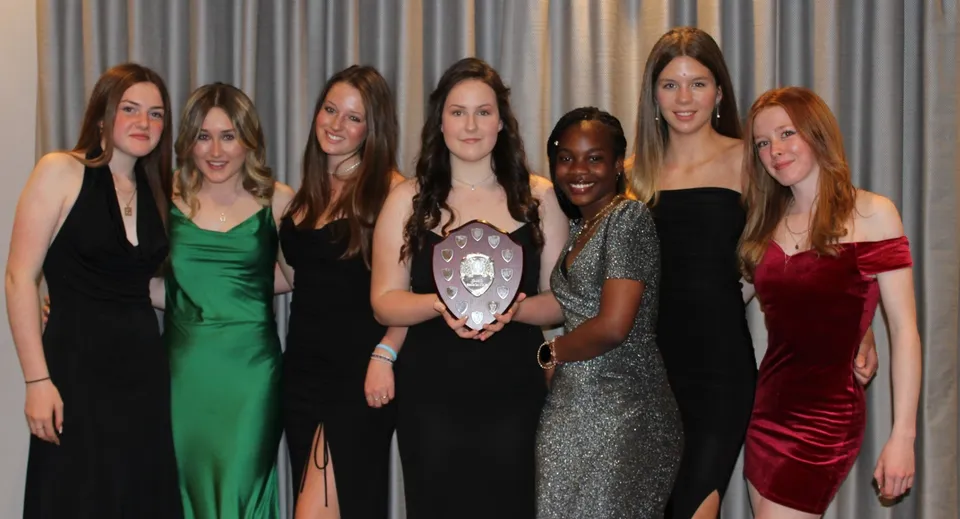 Un gruppo di donne in abito formale posa insieme davanti a una tenda grigia nel campus della Sibford School.