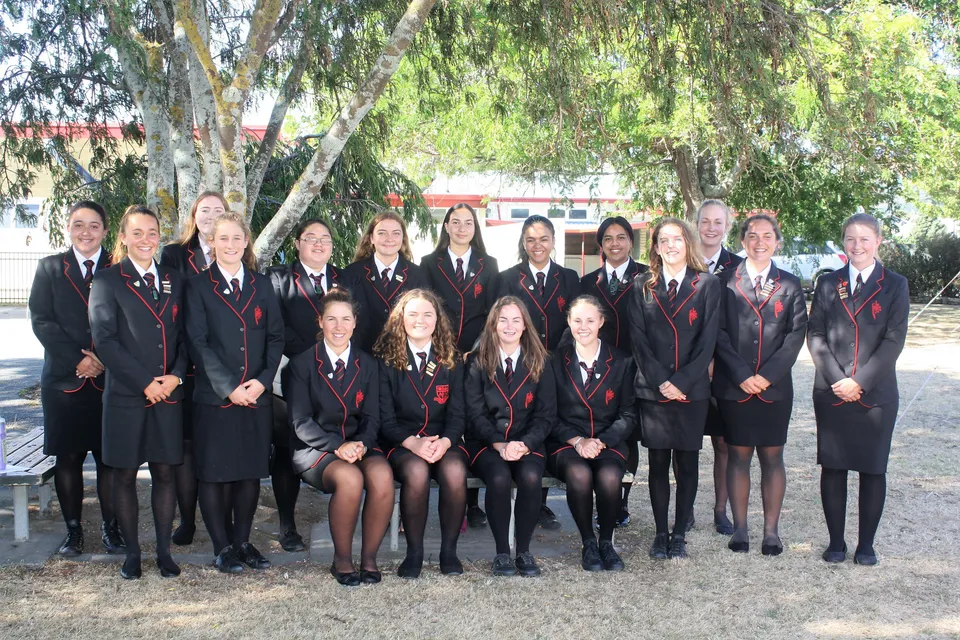Un gruppo di studentesse della Gisborne Girls' High School posa insieme all'aperto tra alberi verdi.