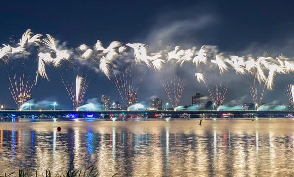 Fuegos artificiales blancos sobre un puente iluminando el cielo nocturno y el agua