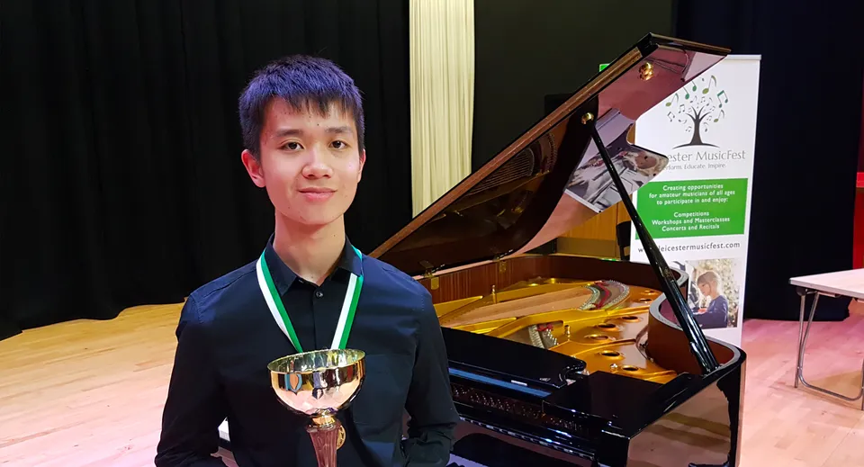 Uno studente della Chase Grammar School è davanti a un pianoforte a coda e tiene in mano una coppa.