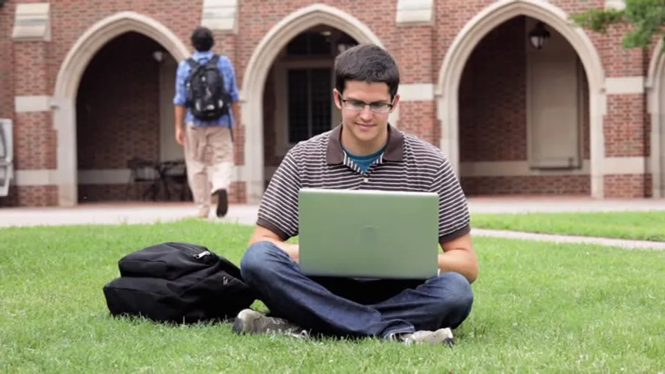 Uno studente della Richmond High School è seduto sull'erba davanti a un edificio in mattoni e lavora su un laptop.