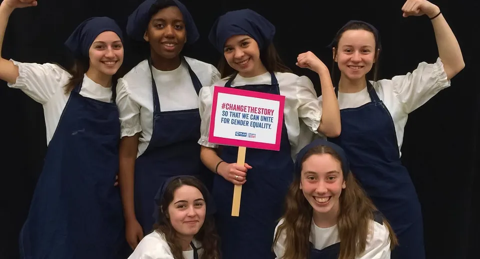 Studentesse della Notre Dame High School manifestano insieme in un ambiente scuro con un cartello in mano.