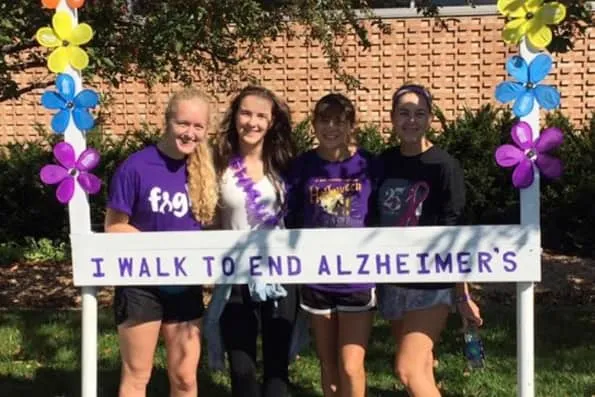 Cuatro jóvenes posan tras un marco con flores y el texto I WALK TO END ALZHEIMER'S