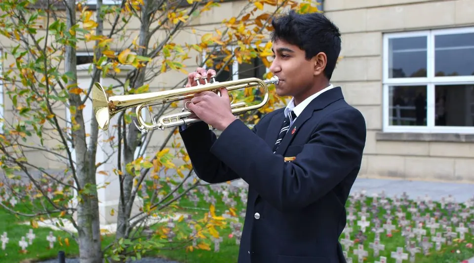Uno studente della St. Paul’s School suona uno strumento a fiato in ottone davanti a uno scenario autunnale e a un edificio scolastico.