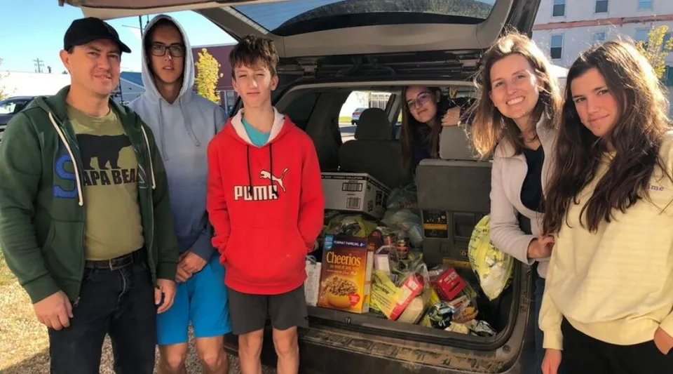 Un gruppo di giovani e adulti della Viking School posa accanto al bagagliaio aperto di un'auto pieno di generi alimentari.