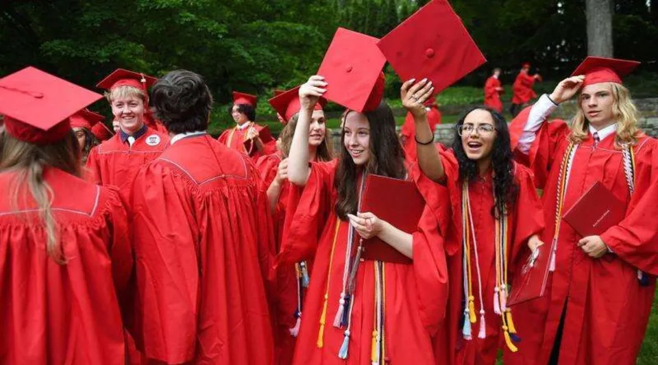 I diplomati della Saint Bernard School festeggiano all'aperto indossando toghe rosse e tenendo in alto i loro diplomi.