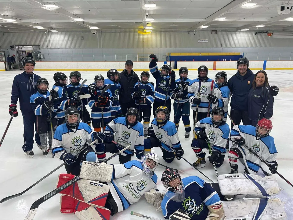 Un gruppo di giovani giocatori e giocatrici di hockey posa sulla pista di ghiaccio della École secondaire publique Carrefour Jeunesse.